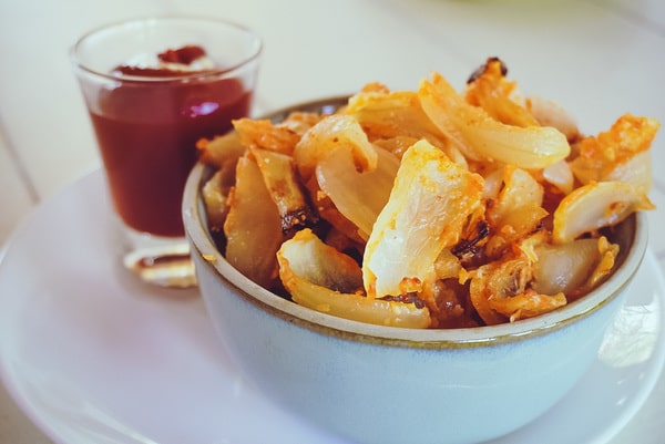 close up of onion strings in a blue bowl with ketchup