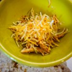buffalo chicken and shredded cheese in a green bowl