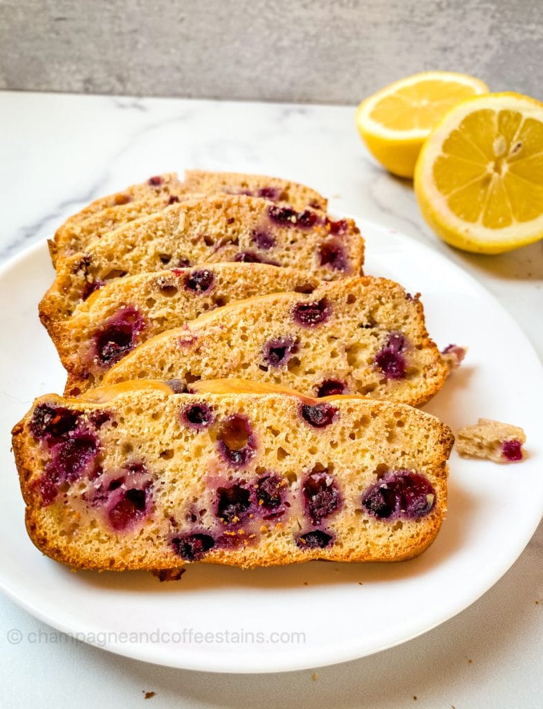 slices of lemon blueberry bread on a white plate with lemons in the background