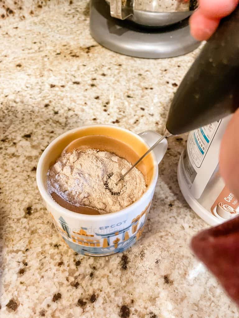 mixing protein powder into a coffee cup with a milk frother