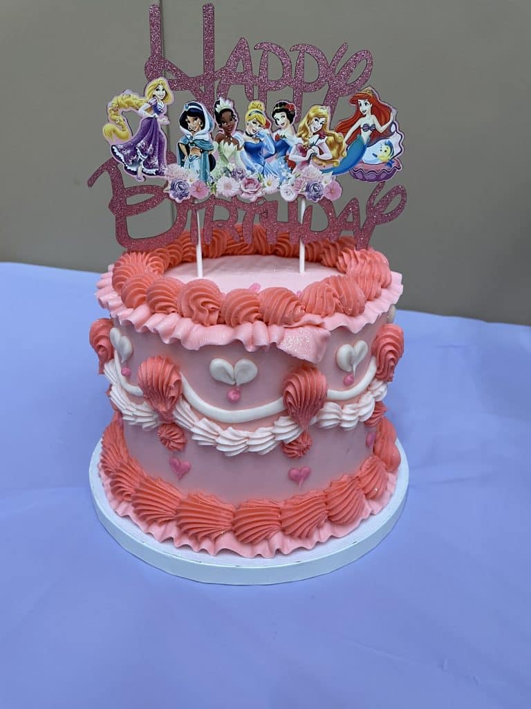 pink birthday cake on a table with disney princesses on top