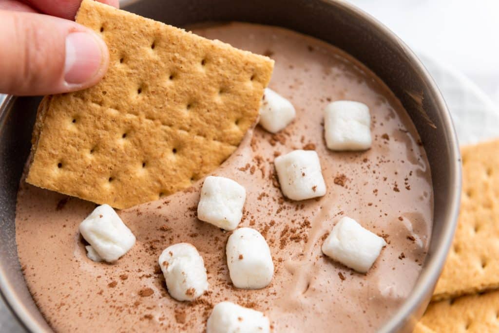 a graham cracker being dipped into hot cocoa dip
