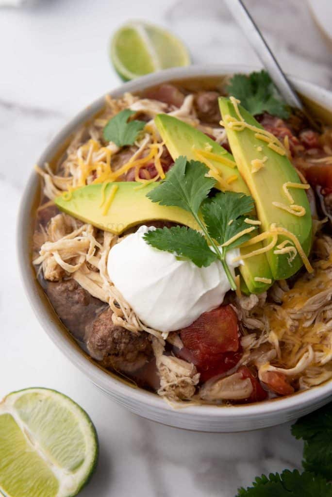 slow cooker chicken taco soup in a bowl with avocado, cheese and sour cream on top